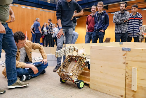 During the STI robot competition, five teams of three master students from different sections of the STI faculty have to design, build and program a cleaning robot. The realized robots must be able to autonomously move in a 64 m² arena that features obstacles and different terrains, while detecting and gathering empty PET bottles, which should then be brought to a specific recycling area. The competition is implemented as a regular semester project during the spring semester.